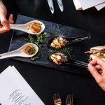 Different types of appetizers in spoons on a serving board.