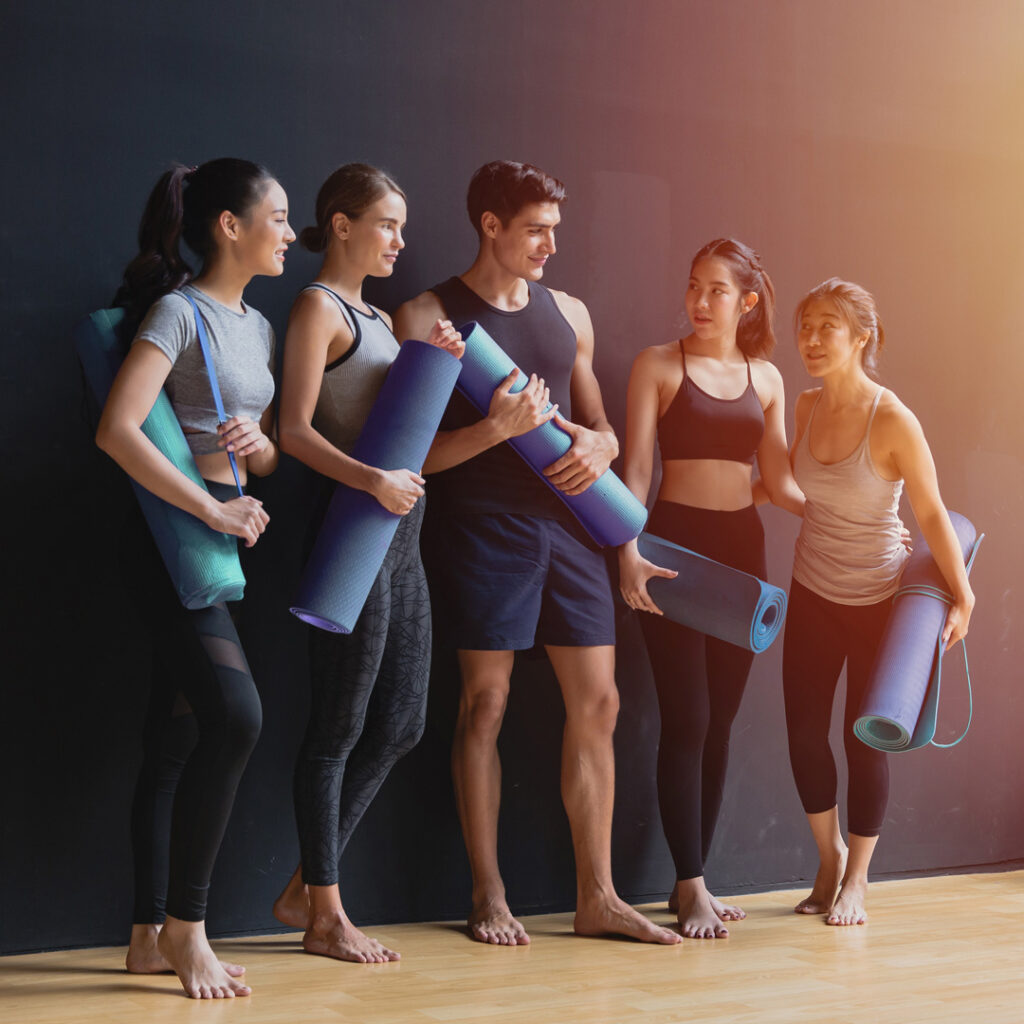 A group of 5 young adults seen holding yoga mats in a studio