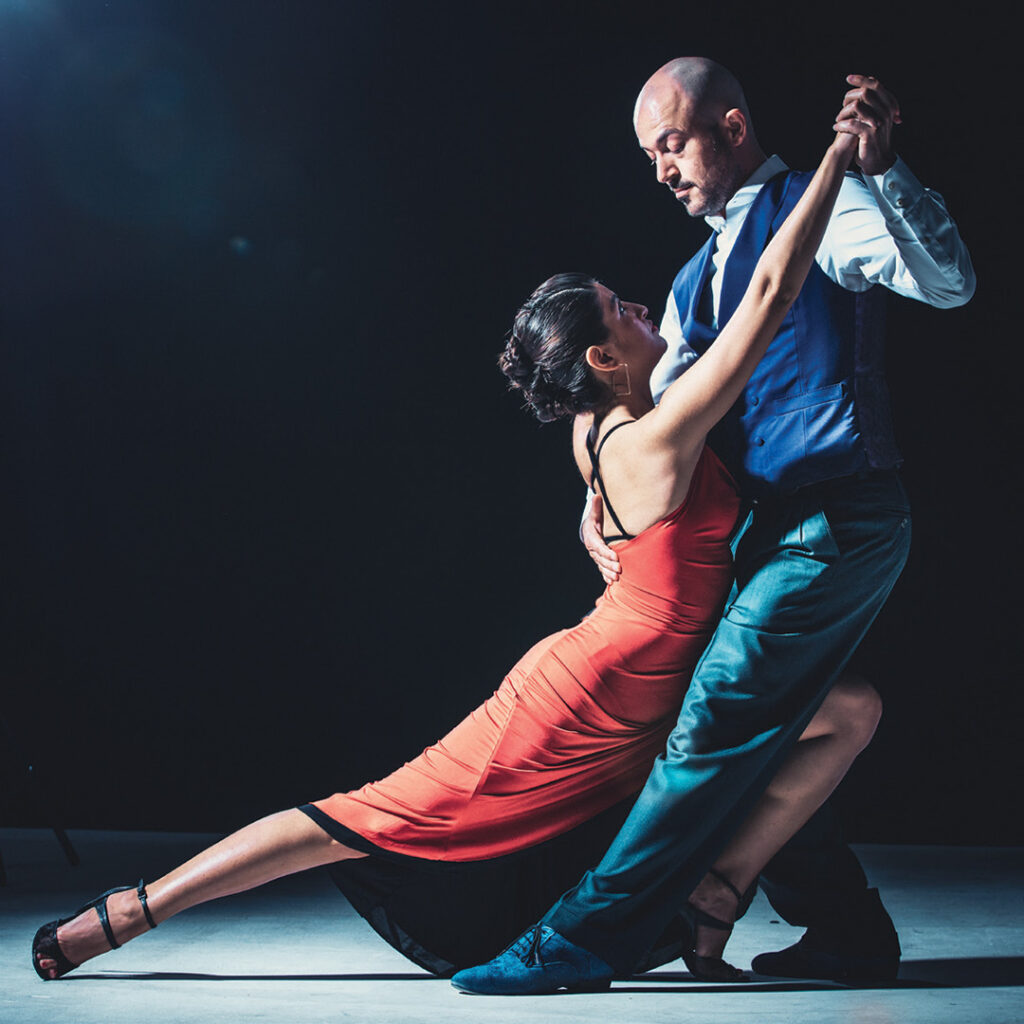 A man and a woman in modern dance costume seen dancing in a studio.