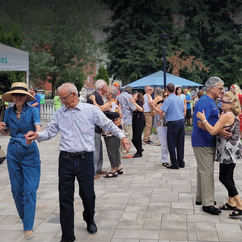 Men and women seen dancing holding hands outdoors on a sunny afternoon