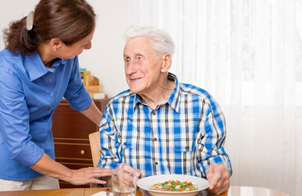 A personal support worker helps a senior with a meal.