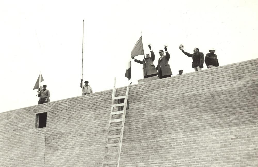 A group of men raising flags at the rooftop ceremony marking the completion of Villa Colombo Toronto's external structure.